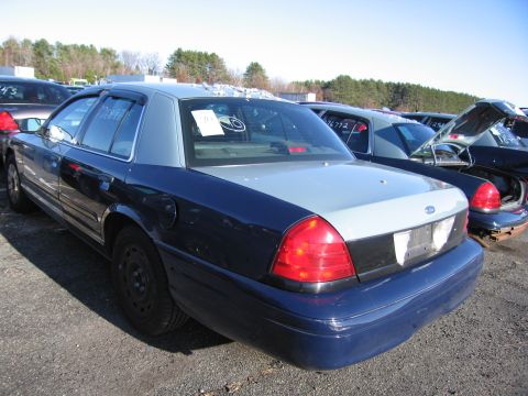 2001 Ford Crown Victoria - A blue and silver 2001 Ford Crown Victoria is seen in a junkyard with other vehicles.