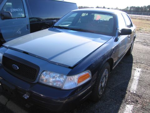 2001 Ford Crown Victoria - A blue Ford Crown Victoria is parked next to a van. The hood is open, revealing the engine bay.