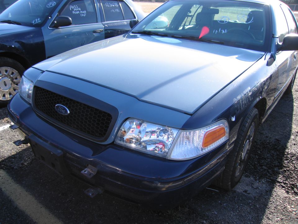 Blue Ford Crown Victoria, front view, showing grille and headlights. Another vehicle is partially visible to the left