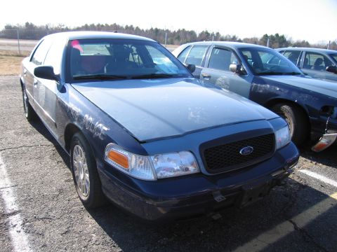 2001 Ford Crown Victoria - A blue police car is parked in a lot next to other similar vehicles.