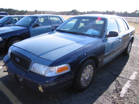 2001 Ford Crown Victoria - A blue 2001 Ford Crown Victoria is parked in a lot with other vehicles, showing markings on its windshield.