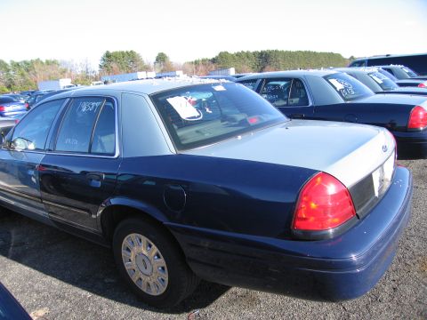 2001 Ford Crown Victoria - A row of Ford Crown Victorias are parked in an outdoor lot under a bright sky.