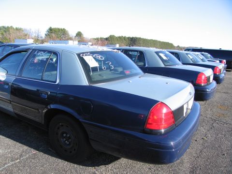 2001 Ford Crown Victoria - Several dark blue and light blue sedans are parked in a lot, with handwritten markings on the rear windows.
