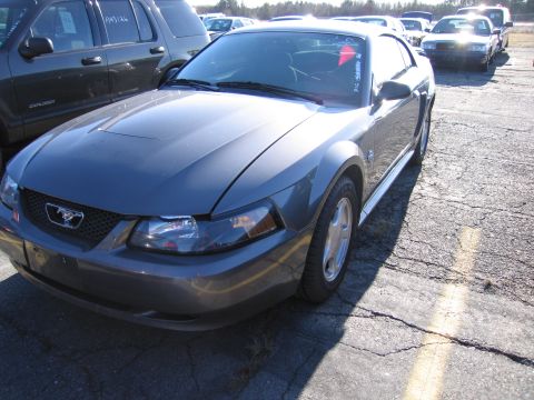 2001 Ford Crown Victoria - A gray Ford Mustang is parked in an outdoor lot next to a dark SUV.
