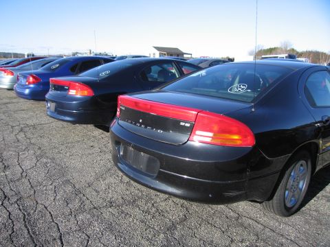 2001 Ford Crown Victoria - A line of sedans, including a black Dodge Intrepid, are parked on an asphalt lot under a clear blue sky.