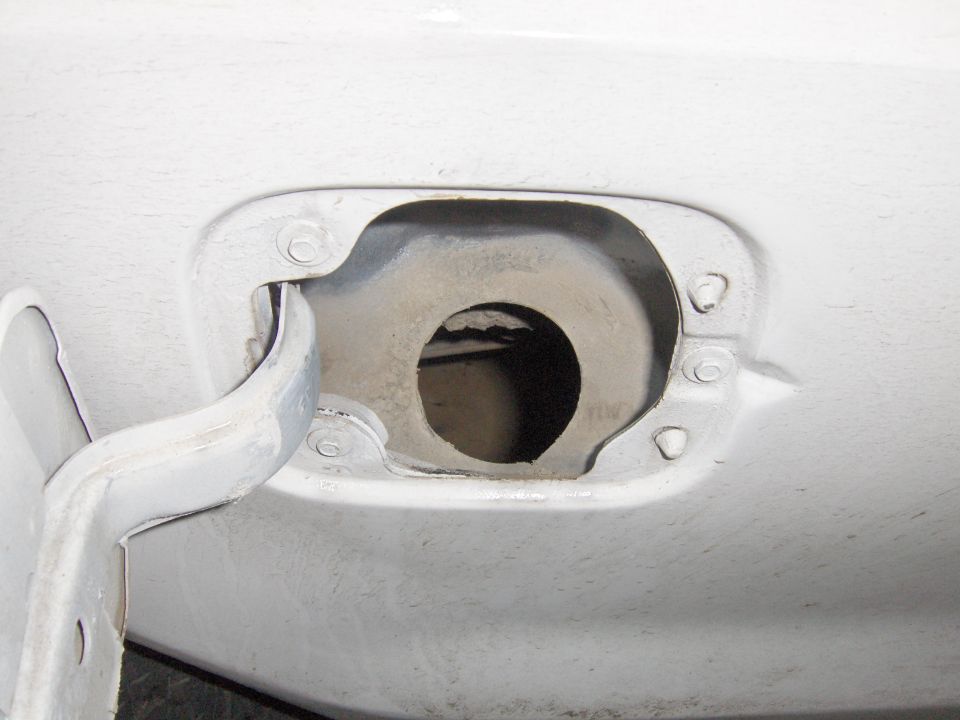 Open white fuel filler door with exposed filler neck and no gas cap