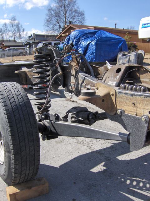 1990 Ford Bronco - Frame and suspension components of a Ford Bronco, with a tarp-covered vehicle in the background.