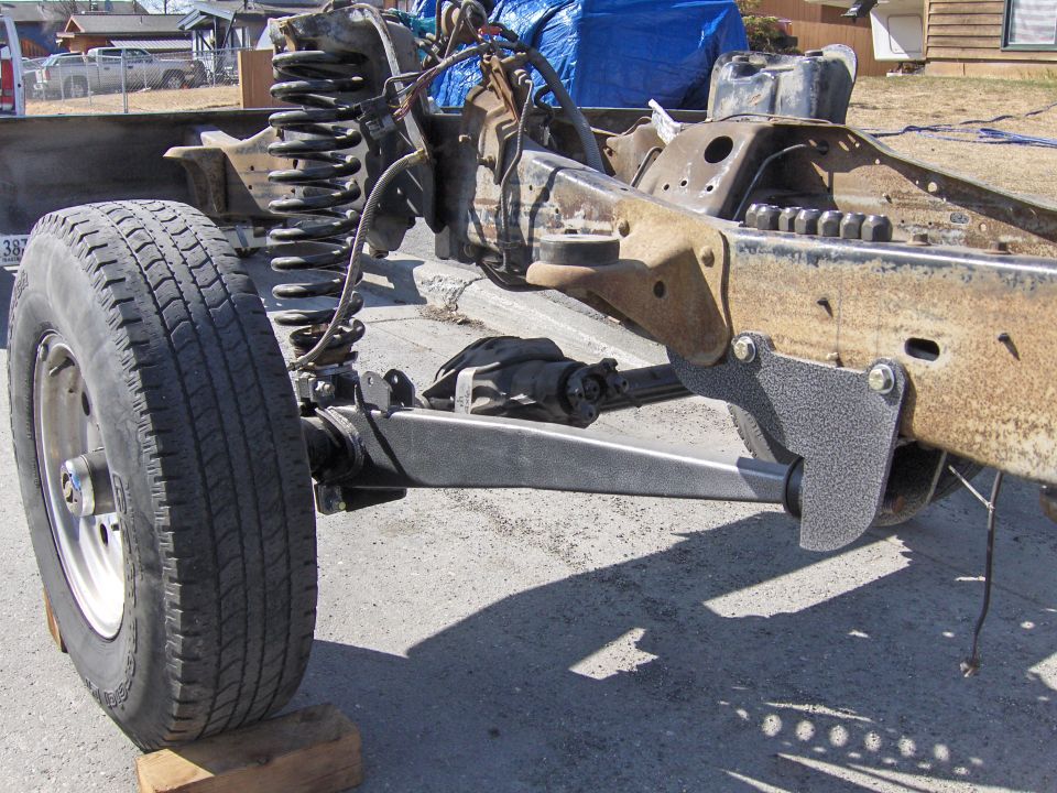 Close-up of a vehicle's front suspension and frame, showing the axle and coil spring assembly