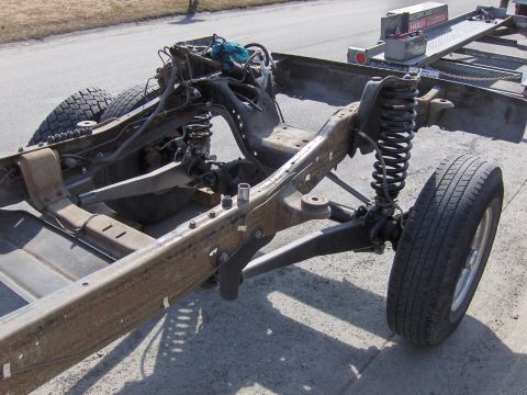 1990 Ford Bronco - Close-up of a vehicle's chassis and suspension system, with a trailer in the background.