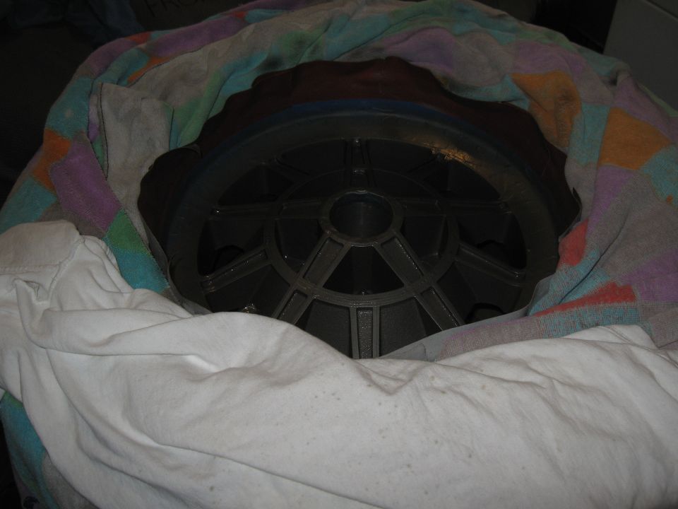 Close-up of a dark gray car wheel with a complex spoke pattern, partially covered by fabric.