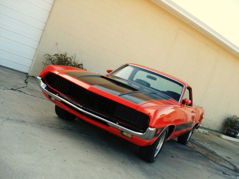1970 Ford Ranchero - Front 3/4 view of a bright red 1970 Ford Ranchero GT with black racing stripes on the hood.