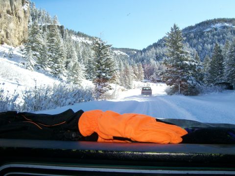 1979 Ford Bronco - An SUV travels down a snow-covered road, surrounded by snow-laden trees and mountains under a clear blue sky.