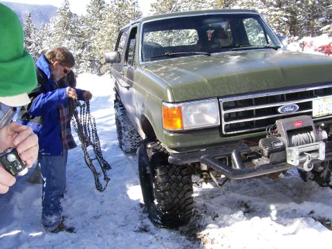 1979 Ford Bronco - A green Ford Bronco is parked in the snow, with people nearby handling tire chains.