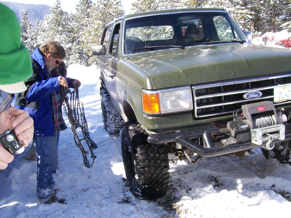 Green Ford Bronco with winch in snow, people preparing chains