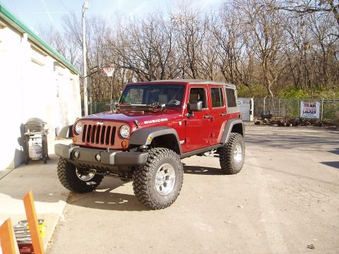 1978 Ford Bronco - A red Jeep Wrangler Rubicon is parked in front of a building with a basketball hoop in the background.