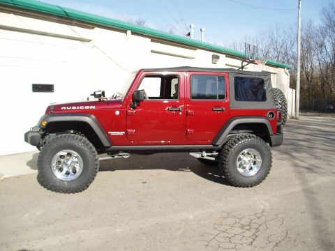 1978 Ford Bronco - A red Jeep Wrangler with a soft top and lifted suspension is parked on a paved surface next to a building.