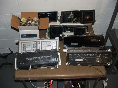 1989 Ford Bronco II - Several automotive dashboard instrument clusters and related parts are laid out on a table, some in boxes.