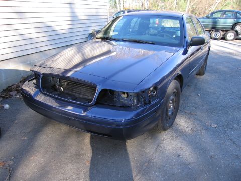1991 Ford LTD Crown Victoria - This blue sedan is missing its headlights and grille, suggesting it is undergoing repairs or has been dismantled.