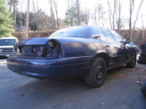 1991 Ford LTD Crown Victoria - The rear of a dark blue sedan is shown with damage and missing taillights, parked outdoors.