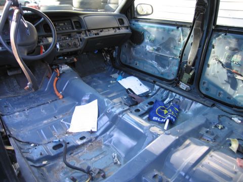1991 Ford LTD Crown Victoria - The interior of a vehicle has been stripped down, revealing the bare metal floor and door structures.