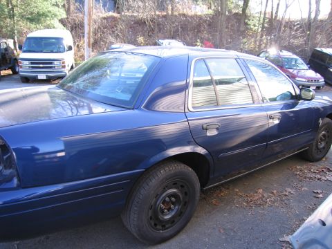 1991 Ford LTD Crown Victoria - A blue sedan is parked on a paved surface with fallen leaves, showing its side profile and a white van in the background.