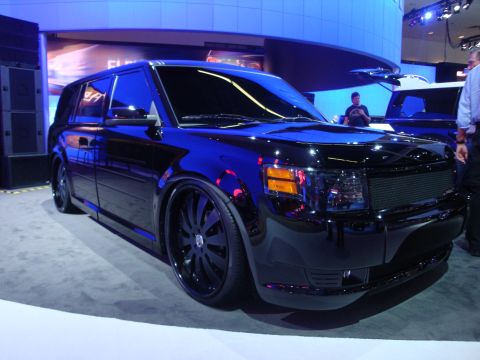 1993 Ford Taurus - Black SUV on display at an auto show with custom wheels and tinted windows.