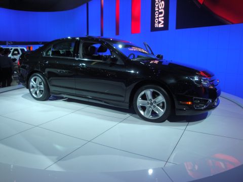 1993 Ford Taurus - A black sedan is displayed on a white platform with a "2010 Ford Mustang" banner visible in the background.