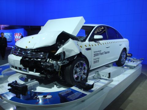 1993 Ford Taurus - A white sedan, identified as a 2008 Ford Taurus, is displayed with significant front-end damage from a crash test.