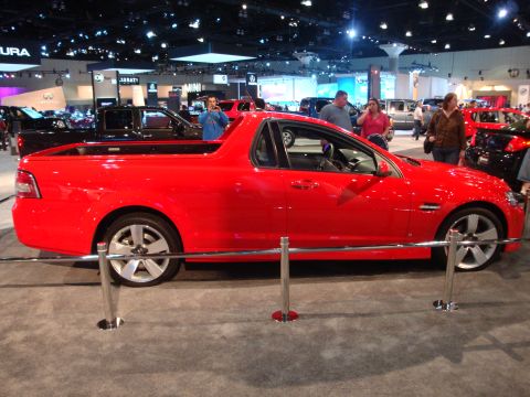 1993 Ford Taurus - A red utility vehicle is displayed at an auto show with other vehicles and attendees in the background.