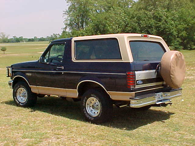 Dark blue and tan Ford Bronco with tan top and covered rear spare tire parked on grass