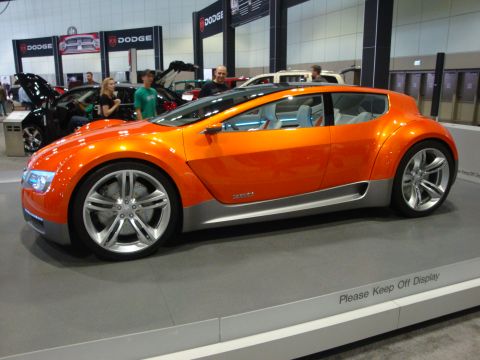 1993 Ford Taurus - An orange concept car is displayed at an auto show with Dodge branding in the background.