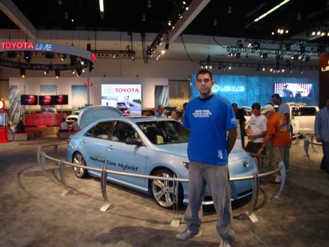 1993 Ford Taurus - A light blue sedan, identified as a Natural Gas Hybrid, is displayed at a car show with a man standing next to it.