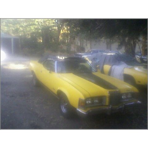 1973 Mercury Cougar - A yellow 1973 Mercury Cougar is parked next to another covered vehicle.