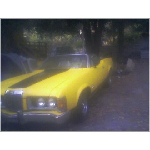 1973 Mercury Cougar - A yellow 1973 Mercury Cougar convertible is parked outdoors, black racing stripes on the hood.