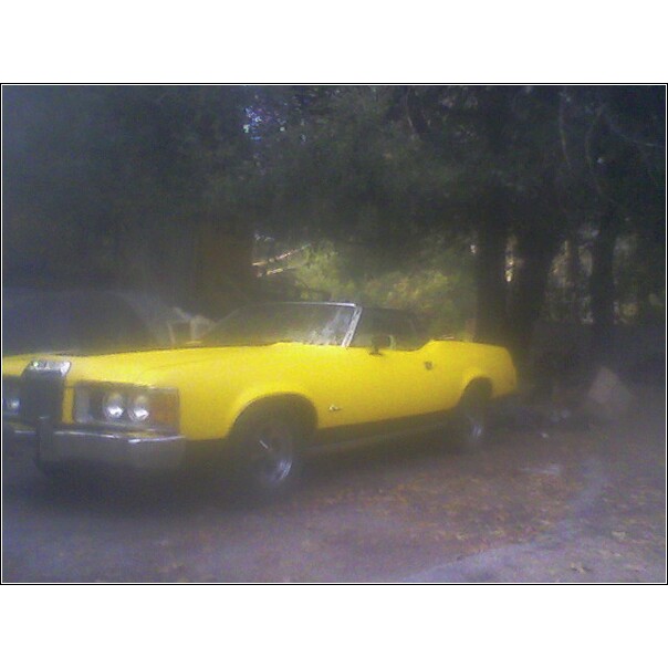 Yellow 1973 Mercury Cougar convertible parked on dirt road with trees in background