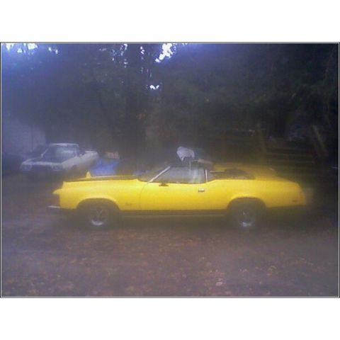 1973 Mercury Cougar - A yellow 1973 Mercury Cougar convertible is parked outdoors next to another vehicle.