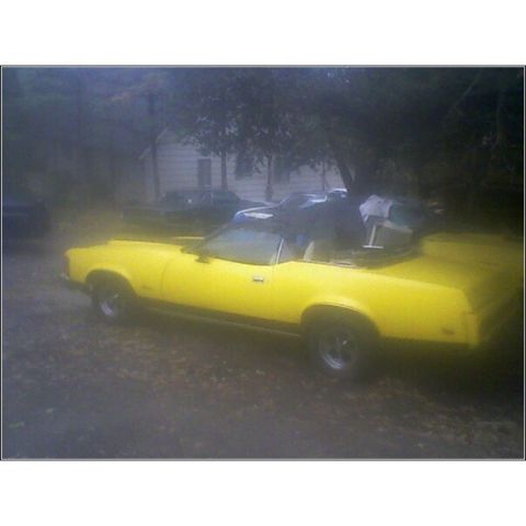 1973 Mercury Cougar - A yellow 1973 Mercury Cougar convertible is seen from the side, parked in a lot with other vehicles.