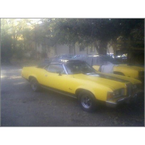 1973 Mercury Cougar - A yellow convertible with a black top and racing stripes is parked outdoors next to another vehicle.