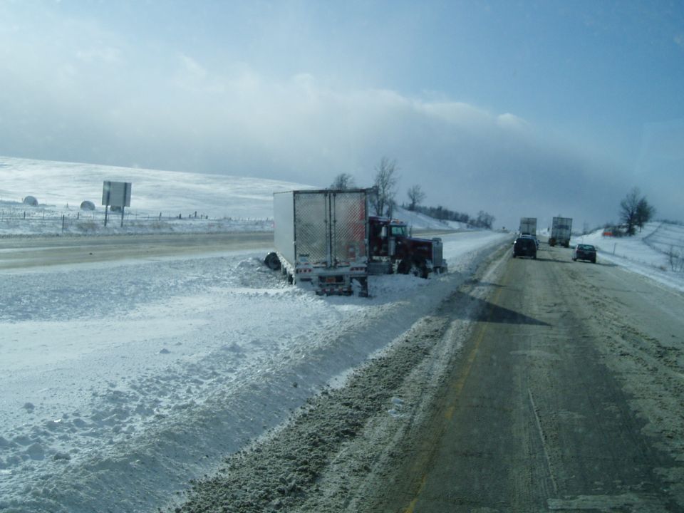 Semi-truck stuck in snow on highway shoulder. Other vehicles on road