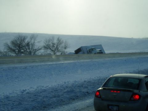 1995 Mercury Grand Marquis - A semi-trailer truck has tipped into a snow-covered ditch on a winter day, as seen from the perspective of a car.