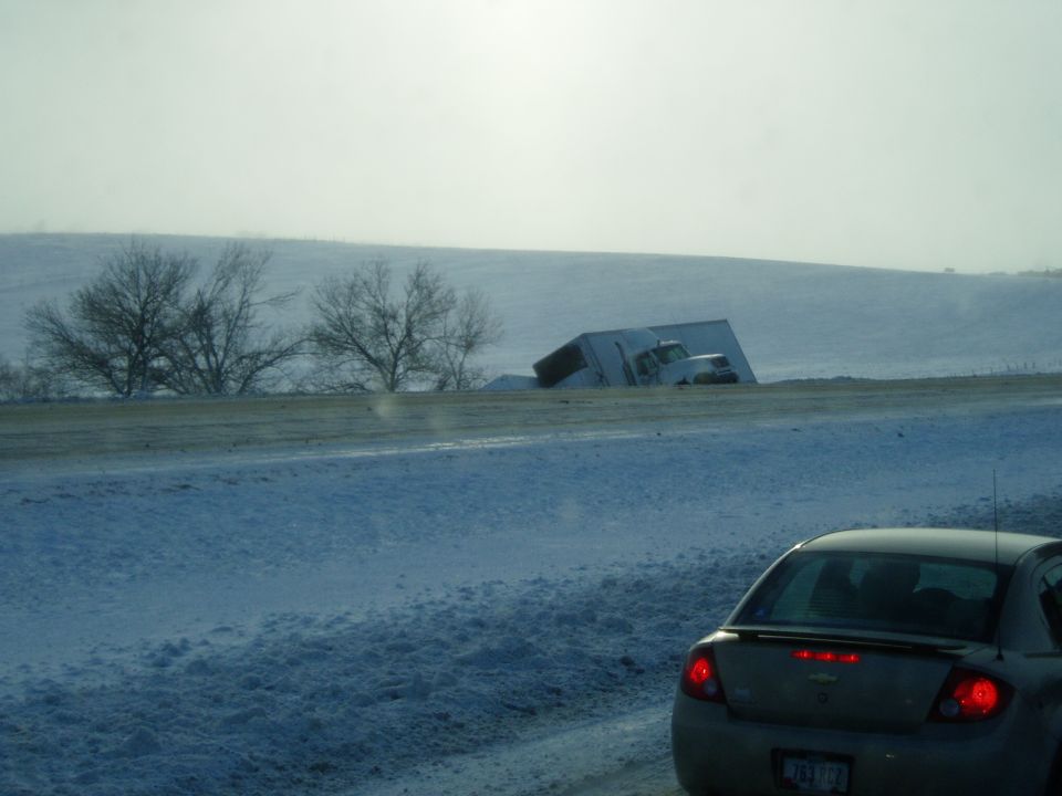 Semi-trailer truck tipped into a snow-covered ditch, seen from a car's interior