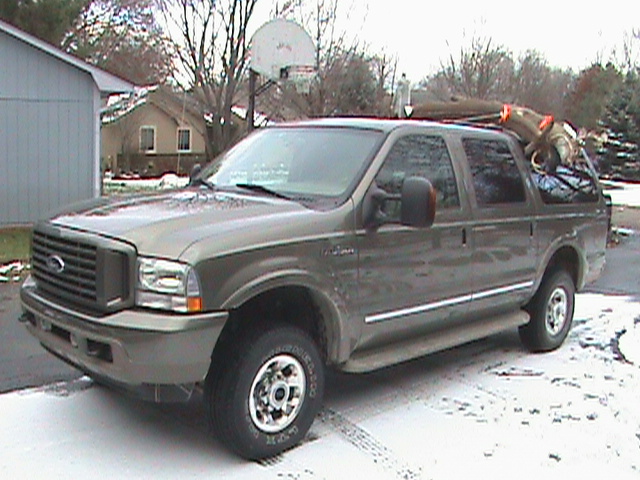Tan Ford Excursion SUV with cargo on roof, parked in snowy driveway, front three-quarter view