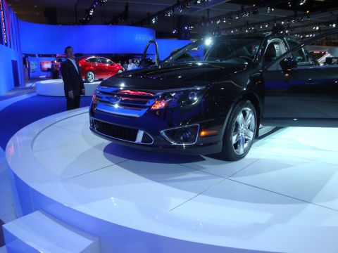1993 Ford Taurus - A black sedan is displayed at an auto show, with a red car visible behind it.