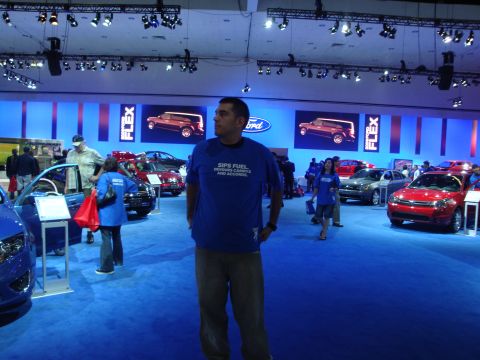 1993 Ford Taurus - A man stands in front of a display of Ford vehicles at an auto show, with the Ford logo and Flex advertisements visible.