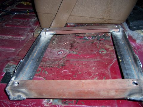 1991 Ford Bronco - Close-up of a metal seat bracket installed on the red floor of a vehicle interior.