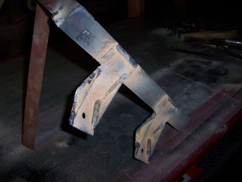 1991 Ford Bronco - A close-up view of a fabricated metal bracket, likely for automotive use, resting on a workbench.