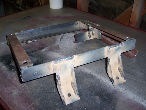 1991 Ford Bronco - A fabricated metal seat bracket, likely for a vehicle, is shown on a workbench. It features welded construction and pre-drilled holes for m…
