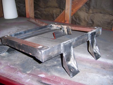 1991 Ford Bronco - A fabricated metal bracket with welded joints and mounting holes sits on a workbench.