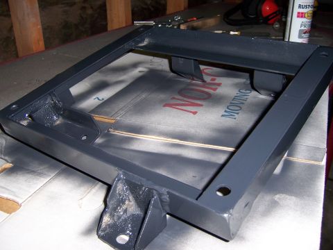 1991 Ford Bronco - A gray metal seat bracket is shown, resting on a cardboard box with visible text.