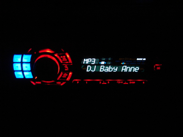 Car stereo displaying "DJ Baby Anne" with blue and red lights